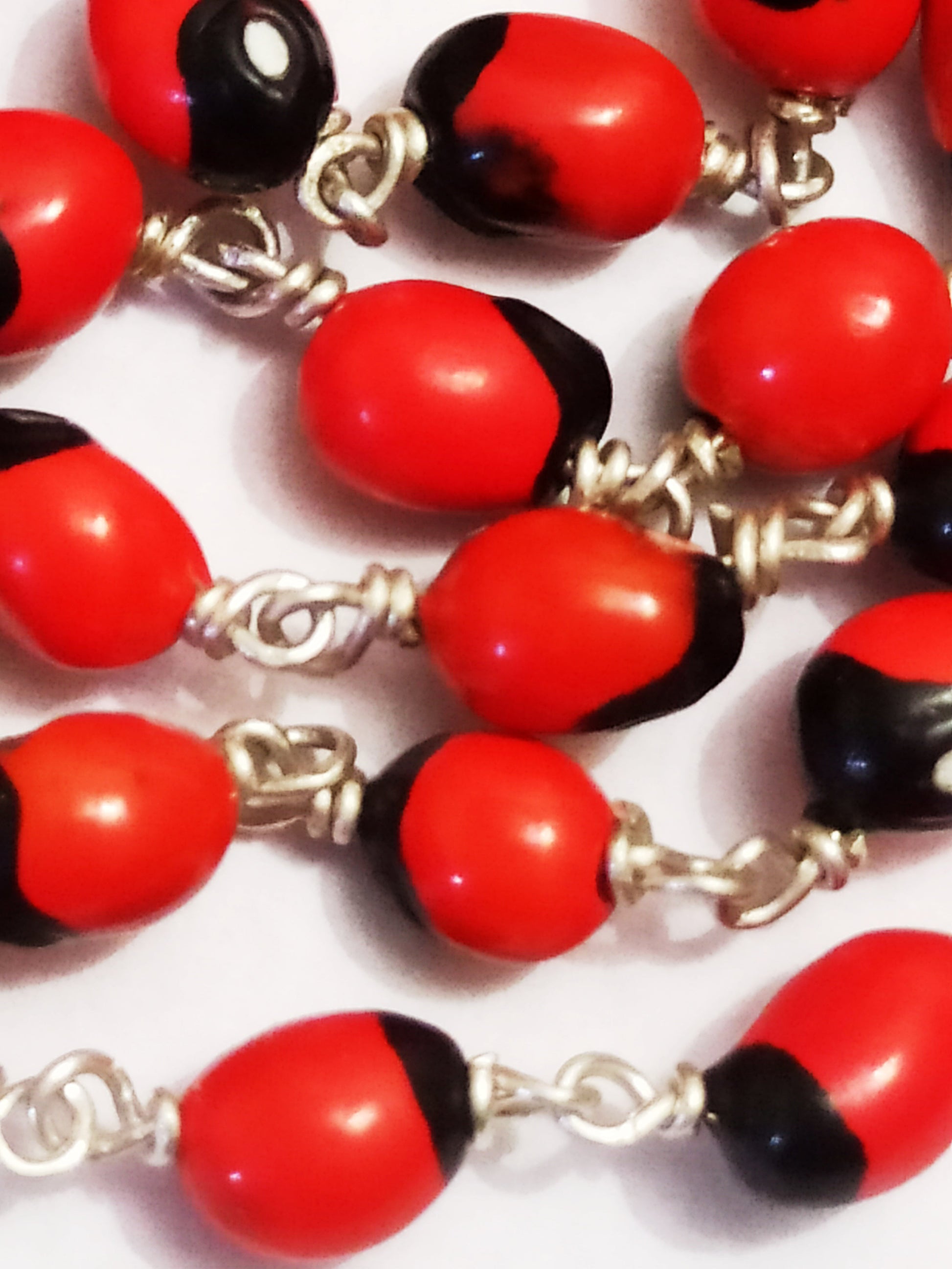 Close-up of red chirmi mala beads with black caps and silver wire chain links