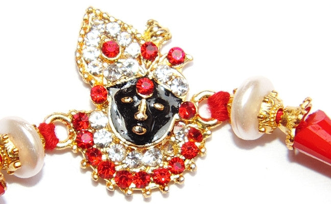 Jeweled Krishna rakhi with red crystals, white pearls, gold accents, red cord ends
