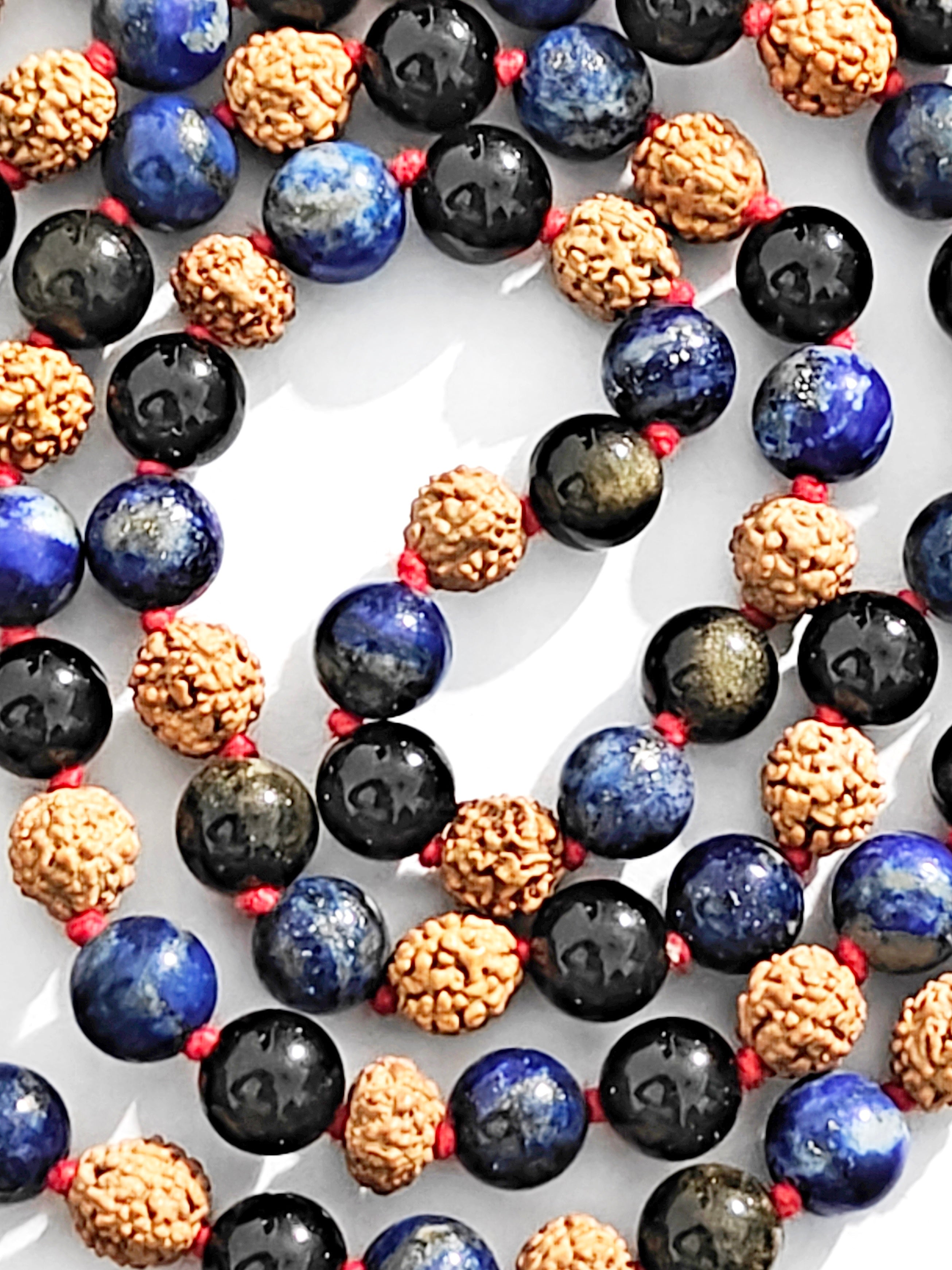 Close-up mala beads: blue lapis, dark black onyx, and gold-textured rudraksha beads