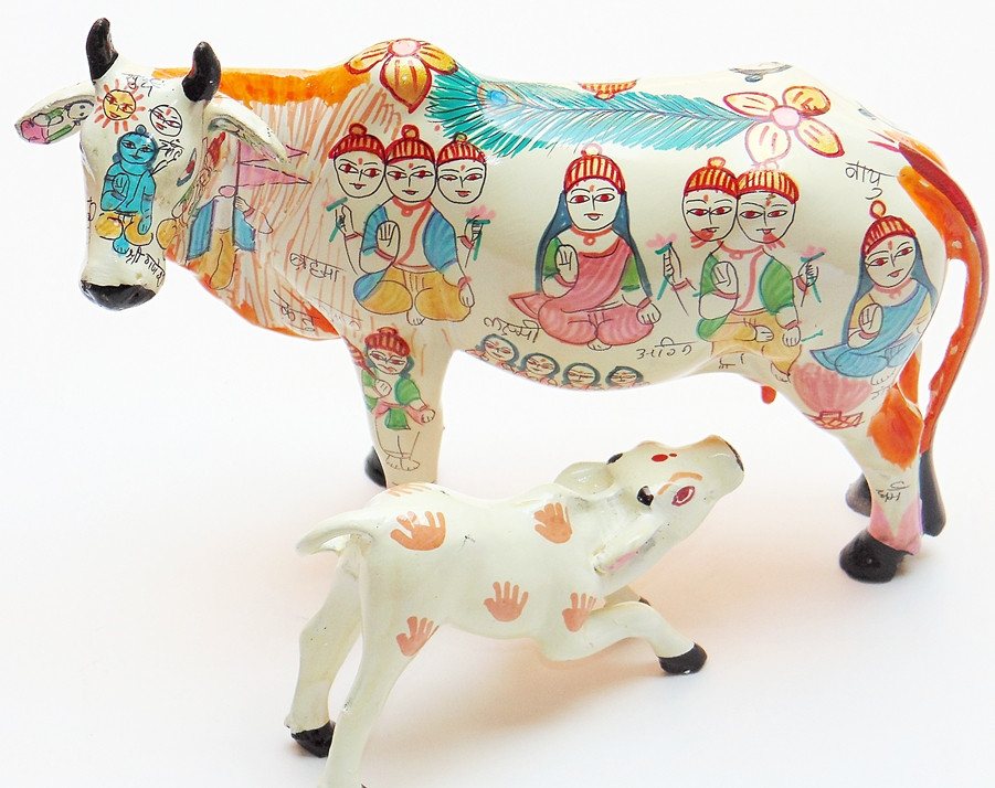 Decorative wish-fulfilling cow figurine with calf, painted faces and patterns, white base.
