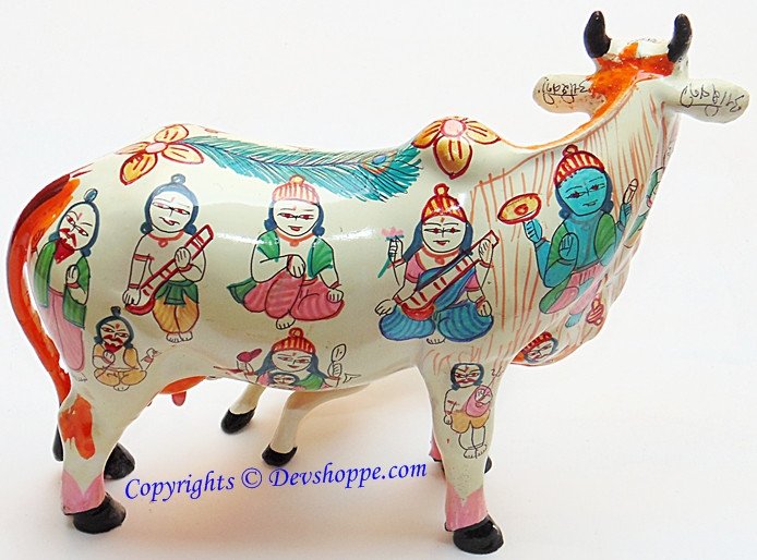 Painted cow idol figurine with colorful traditional figures, white body and black hooves.
