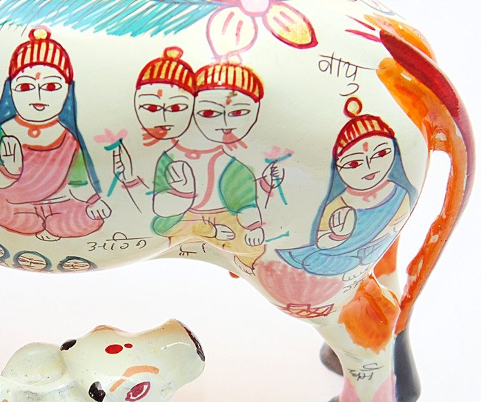 Close-up of painted cow idol side, red-capped faces and blue wing motifs on white body.