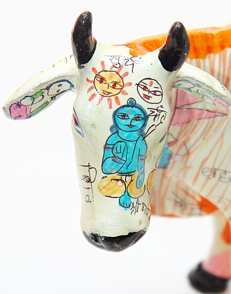 Front view of painted cow idol head, small red mark on white face, black horns.