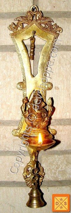 Wall-mount brass lamp with ornate frame and lit diya; Ganesha figure at center