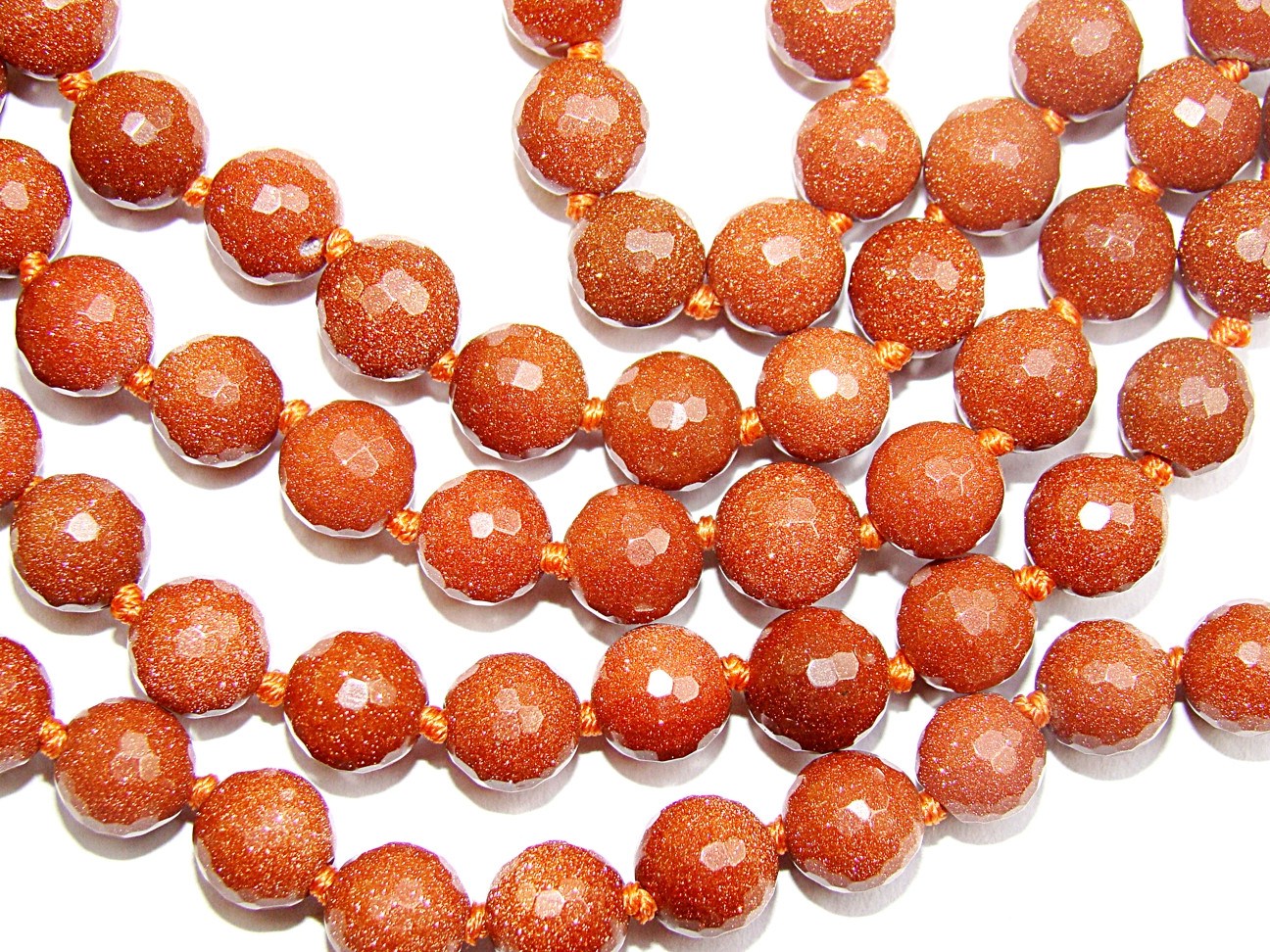 Close-up of orange-red faceted sunstone beads with glossy reflective facets