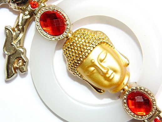Gold Buddha face ornament with red jewel accents on white loop, close-up