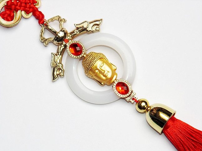 Buddha face hanging ornament with red tassel, gold details, and dangling charms