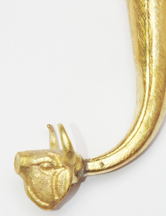 Detailed view of gold animal-head finial at the end of the curved spout
