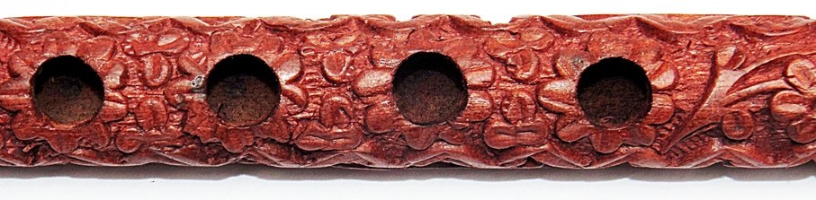Reihe von Tonlöchern auf der Holzflöte, rotbraunes geschnitztes Relief mit Muster