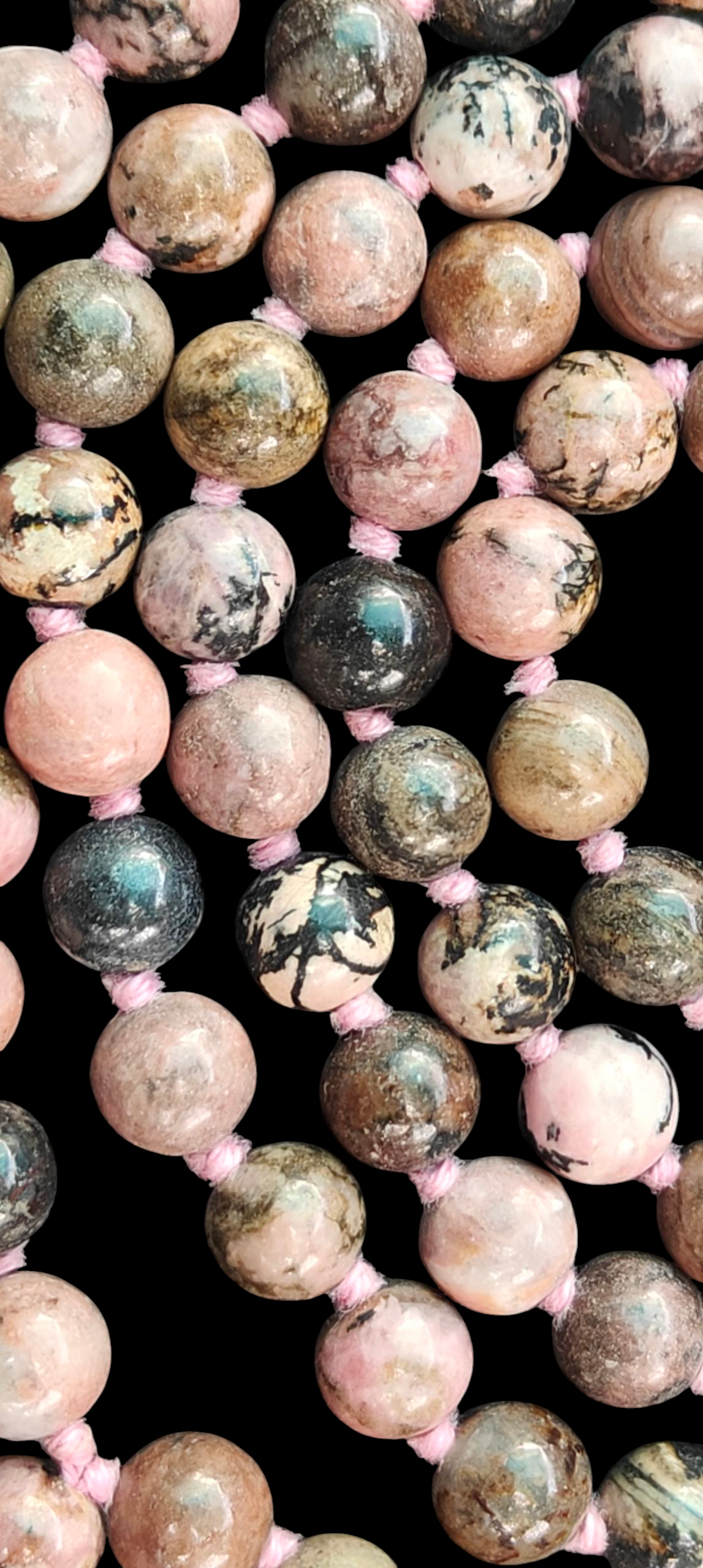 Close-up of rhodonite mala beads: round speckled pink, gray, and teal stones with pink ties