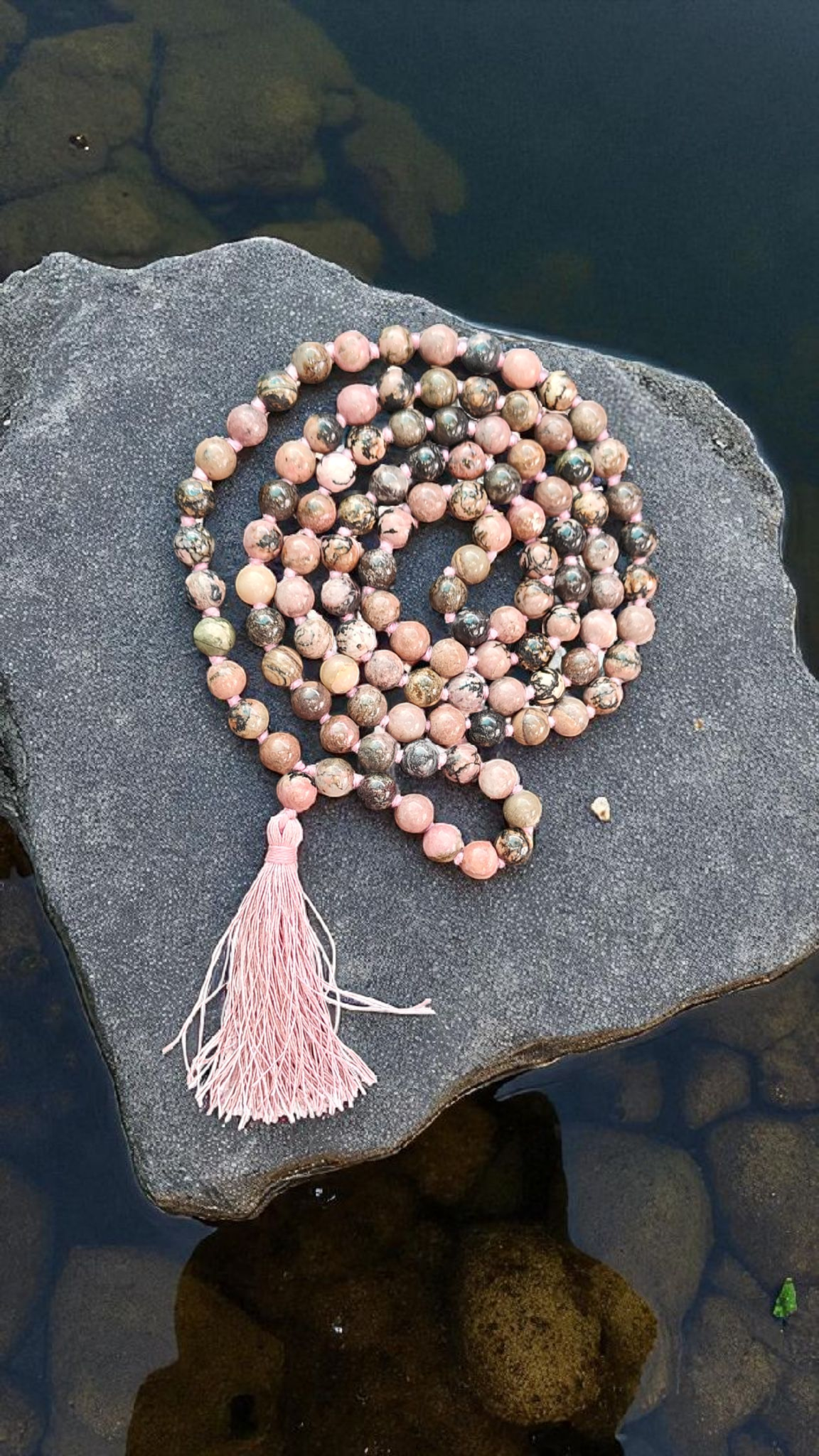 Rhodonite mala on dark stone: layered strand of round pink and teal speckled beads, pink tassel