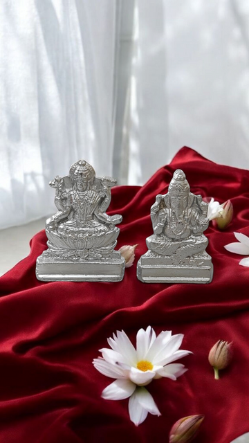 Silver Lakshmi and Ganesha statue pair on red cloth, with small lotus flowers