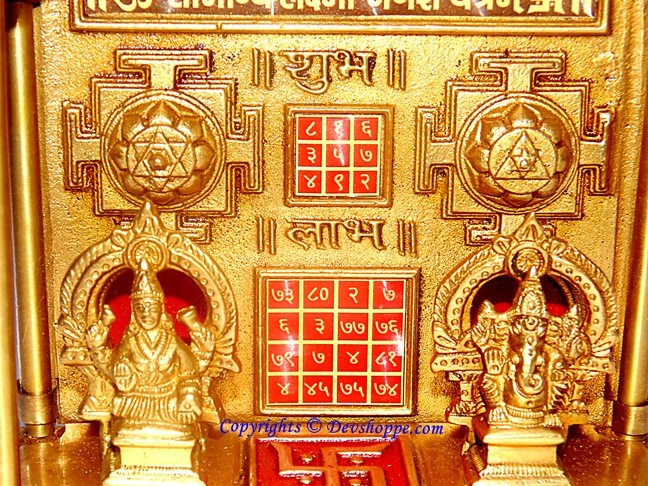 Close view of brass yantra chowki: Lakshmi and Ganesha panels with red symbols